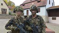 Zwei Soldaten mit Helm, Tarnschminke und Waffen stehen nebeneinander.