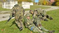 Zwei Soldaten schleifen einen verwundeten Kameraden in eine Deckung.