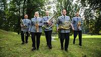 Fünf Militärmusiker gehen auf einer grünen Wiese