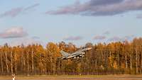 Ein Eurofighter Startet von einer Startbahn, im Hintergrund herbstliche Bäume