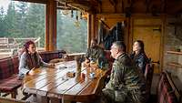 Zwei Soldaten sitzen mit zwei Frauen an einem Tisch im LOT-Haus welches einer Blockhütte ähnelt.