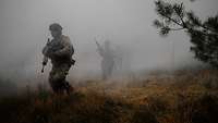 Auf einer Waldlichtung rennen vier Soldaten durch den dichten grauen Nebel.