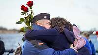 Ein Soldat in Uniform umarmt eine Frau mit Rosen in der Hand