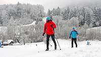 Zwei Sportler fahren auf Skiern durch ein verschneites Gelände