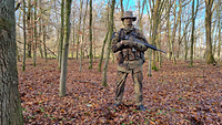 Ein Soldat steht mit seiner Waffe und seiner Ausrüstung im Wald.