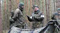 Zwei Soldaten mit Gesichtstarnung unterhalten sich. Einer trägt weiße Armbinden.