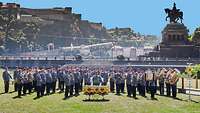 Militärmusiker mit ihren Instrumenten auf einer Wiese vor einer Bergkulisse mit einer Festung