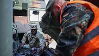 A German and a US soldier inspect the engine compartment of a vehicle