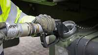 A soldier holds a fuel hose up to a military vehicle