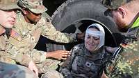 A soldier with a bandaged head lies on the ground. Two other soldiers assist her.