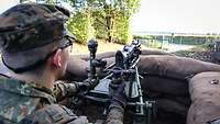 A soldier watches a road. He stands behind sandbags holding a weapon