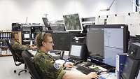 Ein Soldat beobachtet mehrere Monitore und bedient ein Funkgerät.