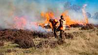 Zwei Männer stehen auf einem Feld, im Hintergrund Feuer