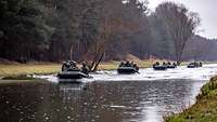 Soldaten in mehreren Schlauchbooten fahren hintereinander auf einem Fluss.