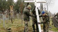 Drei Menschen in Uniform stellen ein weißes Holzkreuz auf