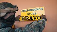 Ein Soldat befestigt ein Schild mit der Aufschrift „Gefährdungsstufe Bravo“ an einer Wand