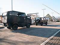 Zwei Militärfahrzeuge fahren auf einer Straße durch eine geöffnete Schranke aus dem Kasernentor