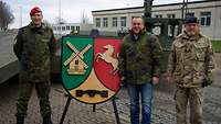 Drei Personen stehen neben einem aufgestellten Wappen