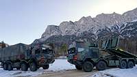 Zwei in tarnfarben lackierte militärische Fahrzeuge stehen sich gegenüber. Im Hintergrund sind Berge zu sehen.