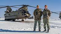 Zwei Soldaten in Uniform stehen im Schnee vor einem Tandemhubschrauber.