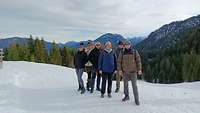 Fünf Menschen stehen auf Schnee, im Hintergrund Berglandschaft