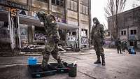 Soldaten in Schutzkleidung und -masken laufen durch Wannen mit Flüssigkeit zur Dekontamination.