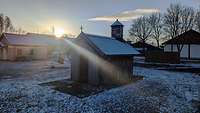 Eine kleine Holzkapelle, von hinten scheint die Sonne auf die Kapelle