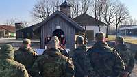 Im Vordergrund Soldaten, die zu den Pfarrern schauen, die vor der Kapelle stehen