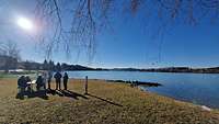 Menschen picknicken an einem See bei strahlend blauem Himmel und Sonnenschein.