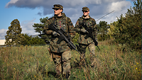 Zwei Soldaten stehen bewaffnet auf einem Feld