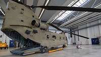 Ein Militärhubschrauber steht mit geöffneter Heckklappe in einem Hangar.