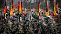 Viele deutsche Soldaten stehen bei einem Appell mit Truppenfahnen auf einem Platz in Formation.