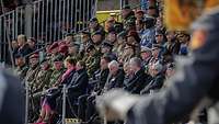 Soldaten und Zivilisten sitzen auf einer großen Tribüne.