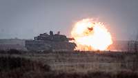 Auf einer Fläche steht ein Panzer und schießt. Ein Feuerball entsteht an der Kanonenmündung.