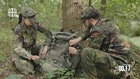 Eine Soldatin und ein Soldat bedienen einen Rucksack hockend im Wald