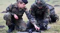 Soldatin kniet neben einem Rekruten und erklärt ihm den Aufbau der Waffe G36