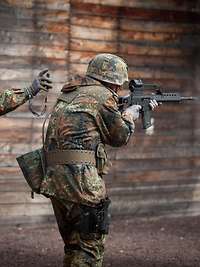 Soldat mit Gewehr im Anschlag, ein weiterer mit Stoppuhr