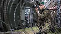 Ein Soldat hinter Stacheldraht fotografiert.