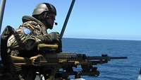 Ein Soldat steht an einer Waffe und schaut auf das offene Meer 