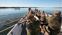 Mehrere Soldaten sitzen in einem Boot und rudern.