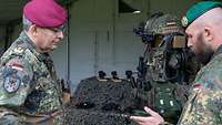 Ein Soldat erläutert einem General die Ausrüstung eines Infanteristen, im Hintergrund Ausrüstung.