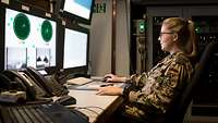 Eine Soldatin der Bundeswehr sitzt an einem Schreibtisch vor drei Monitoren.