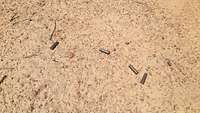 Vier Patronenhülsen liegen auf dem Sandboden
