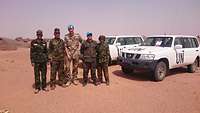 Gruppenbild mit Soldaten, daneben UN-Fahrzeuge