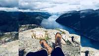 Rebecca sitzt auf einem Felsen. Ihre Beine sind zu sehen. Im Hintergrund erstreckt sich ein norwegischer Fjord.
