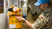 Ein Soldat wirft eine Postkarte in einen Briefkasten der Feldpost im Einsatz.