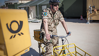 Soldat fährt im Einsatz auf einem Postfahrrad an einem Briefkasten vorbei.