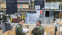 Zwei Soldaten stehen vor Kisten mit Paketen 