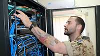 Martin B. steht vor einem großen Tower mit Servern und verkabelt das Netzwerk