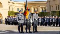 Three service men in basic dress, the one in the middle holds the flagpole with the Federal Institutions Flag